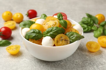 Fresh salad with yellow tomatoes, basil and mozzarella cheese on grey table, closeup