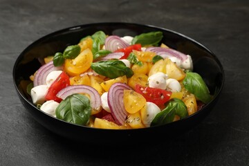Tasty salad with yellow tomatoes, basil, onion and mozzarella cheese on black table, closeup