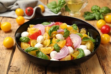 Tasty salad with yellow tomatoes, basil, onion and mozzarella cheese on wooden table, closeup