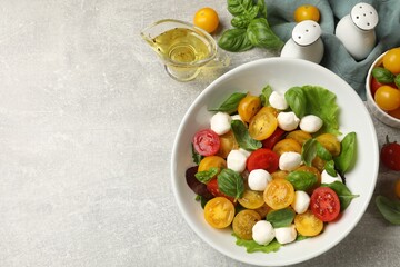 Tasty salad with yellow tomatoes, basil and mozzarella cheese on light grey table, flat lay. Space for text