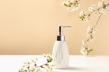 Bottle of cosmetic product and twigs with beautiful flowers on white table against beige background