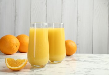 Orange juice in glasses and fresh fruits on white marble table, space for text