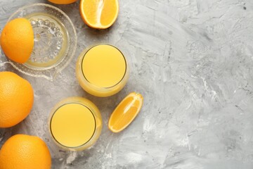 Orange juice in glasses, fresh fruits and juicer on grey table, flat lay. Space for text