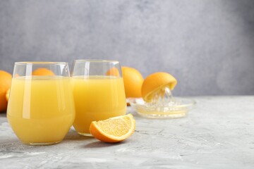 Orange juice in glasses, fresh fruits and juicer on grey table, closeup. Space for text