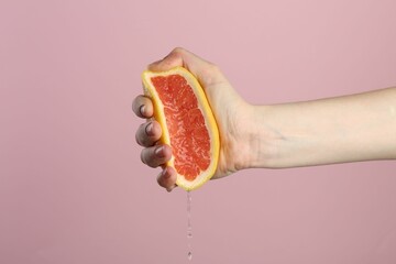 Woman squeezing grapefruit on pink background, closeup