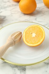 Half of fresh orange and squeezer on white marble table, closeup