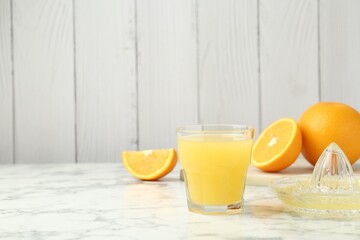Fresh orange juice, fruits and squeezer on white marble table against wooden background, closeup. Space for text