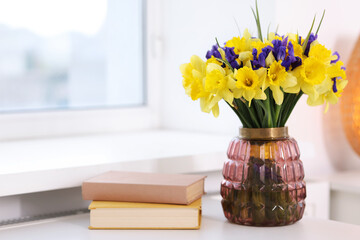 Bouquet of beautiful flowers in vase and books on desk near window indoors