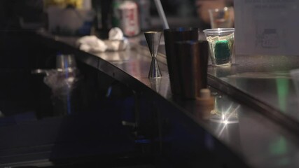 Close-up footage of a bartender shaking and preparing a cocktail behind a lively indoor bar during evening hours. 