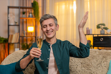 Young man at home lifts champagne glass with a confident smile, celebrating personal success....