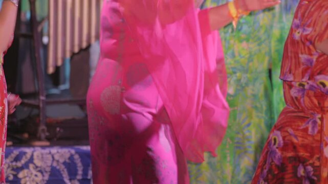 Close-up footage of people in colorful vintage attire&mdash;such as retro kaftans&mdash;dancing under groovy, multicolored lights near a stage. 