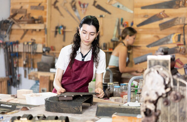 In carpentry workshop, girl master performs work, is engaged in production of wooden decorative...