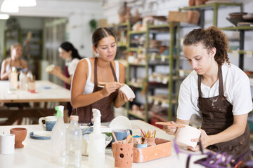 During lesson, guy levels surface of ceramic plate, processes it with spatula, prepares product before decorating and painting. Hand made art, hobbies and creativity.