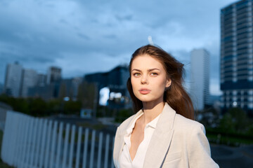 Confident business woman in a city setting, dressed in a light suit, showcasing determination against a modern urban background during twilight.