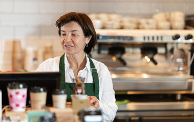 Elderly woman barista in apron at cash register in coffee shop