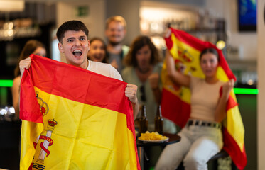 Group of friends fans watching match cheering with Spanish flag in bar