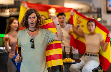 Group of friends fans watching match cheering with flags of Catalonia and Spain in bar