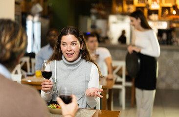 During lunch break, girl at cafe table eats, talks with interlocutor, spends time in company of man. Meeting on neutral territory, discussing personal and business issues during coffee break.