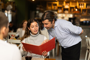 Man listen to restaurant girl customer, writes down order items in phone notes, and records order dish name in mobile application. Waiter of public catering answers customers questions