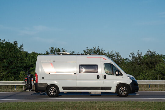 Rollerteam Livingstone 6 camper van based on Fiat Ducato driving along a highway at sunset. Side view with bicycles on the rear and a green landscape in the background. 02.06.2024, Subotica, Serbia