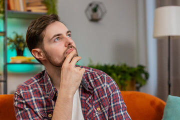 Thoughtful Caucasian man guy sitting at home looks pensive thinks over life concerns or unrequited...