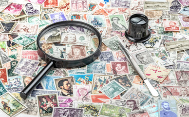 Magnifying glass, tweezers, and monocle on a stamp collection background. Philately concept.