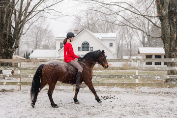young woman riding a horse in the snow with a red sweater