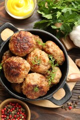 Tasty patties, dill in frying pan, parsley, mustard and peppercorns on wooden table, flat lay