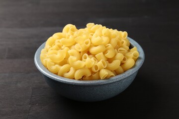 Raw horns pasta in bowl on dark wooden table, closeup