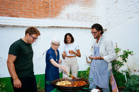 Happy family cooking paella in yard during weekend