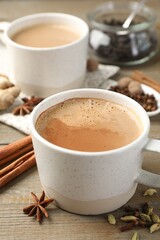 Aromatic Masala tea in cups and spices on wooden table, closeup
