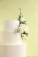 Delicious wedding cake decorated with flowers on light green background, closeup