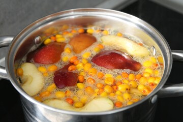 Making compot of apples and sea buckthorn berries. Simmering fruits in pot on stove, closeup