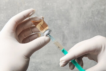 Doctor filling syringe with hepatitis vaccine from glass vial against grey background, closeup