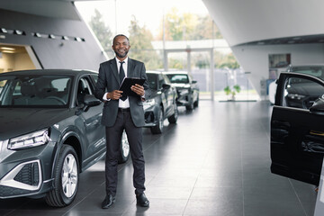 Cheerful sales agent posing among brand-new vehicles in showroom