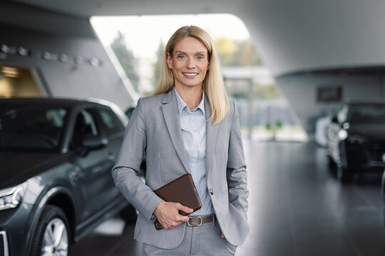 Sales consultant posing while standing among automobiles in showroom