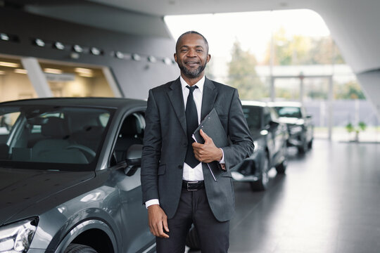 Sales rep posing with clipboard in hand against motorcars in showroom