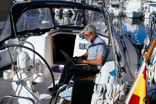 Senior captain working on document with laptop at back of yacht