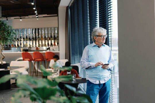 Digital company boss using mobile phone and looking from window