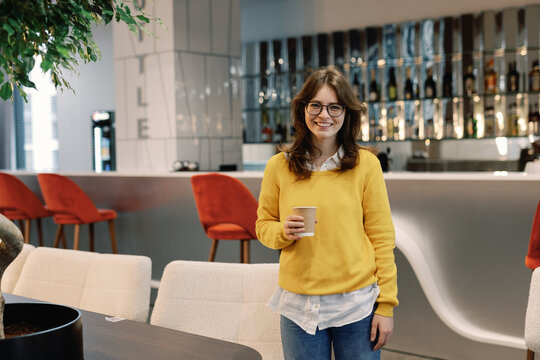Young pleased female digital company employee with coffee cup