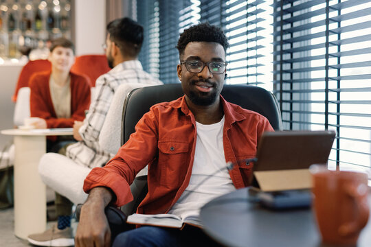 Smiling black IT company employee looking at camera near coworkers - Powered by Adobe