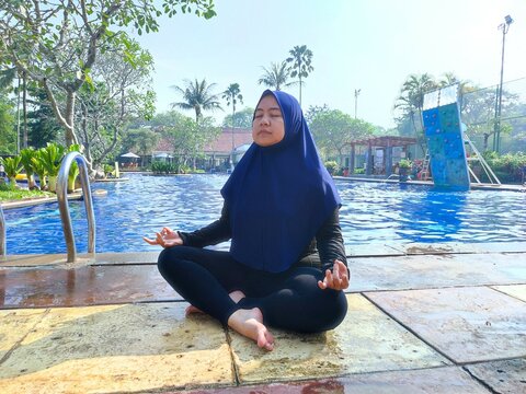 Asian woman in hijab sitting by the pool, meditating with aakash mudra hand position with eyes closed