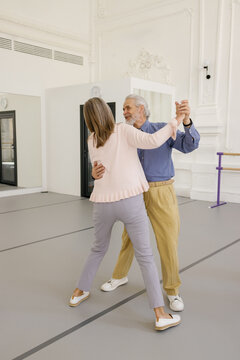 Gray-haired man practising dance moves with partner at dance studio