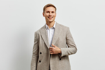 Confident smiling young man in light gray suit with white shirt, casual fashion, standing against...