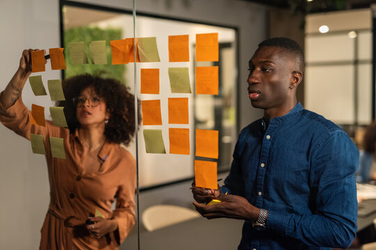 Focused young people putting stickers on glass wall