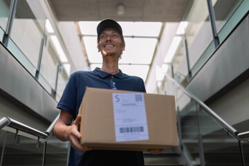 Cheerful deliveryman carrying package in modern building