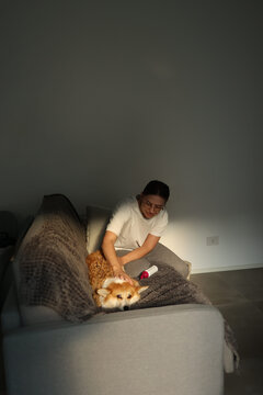 Young woman sitting on couch beside her foxy dog and petting it