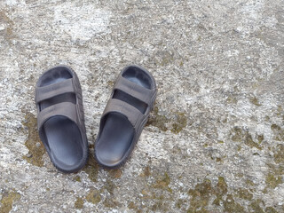 A pair of dirty black rubber sandals, lying on a rough cement surface.
