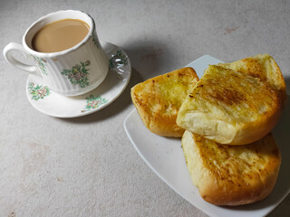 Garlic bread and a cup of warm coffee served on a white plate.