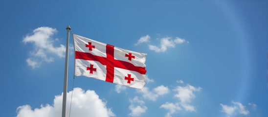 Georgian flag waving proudly against blue sky with clouds. National flag of Georgia blowing in the wind. Patriotism, independence, national symbol of Georgia. 26 May